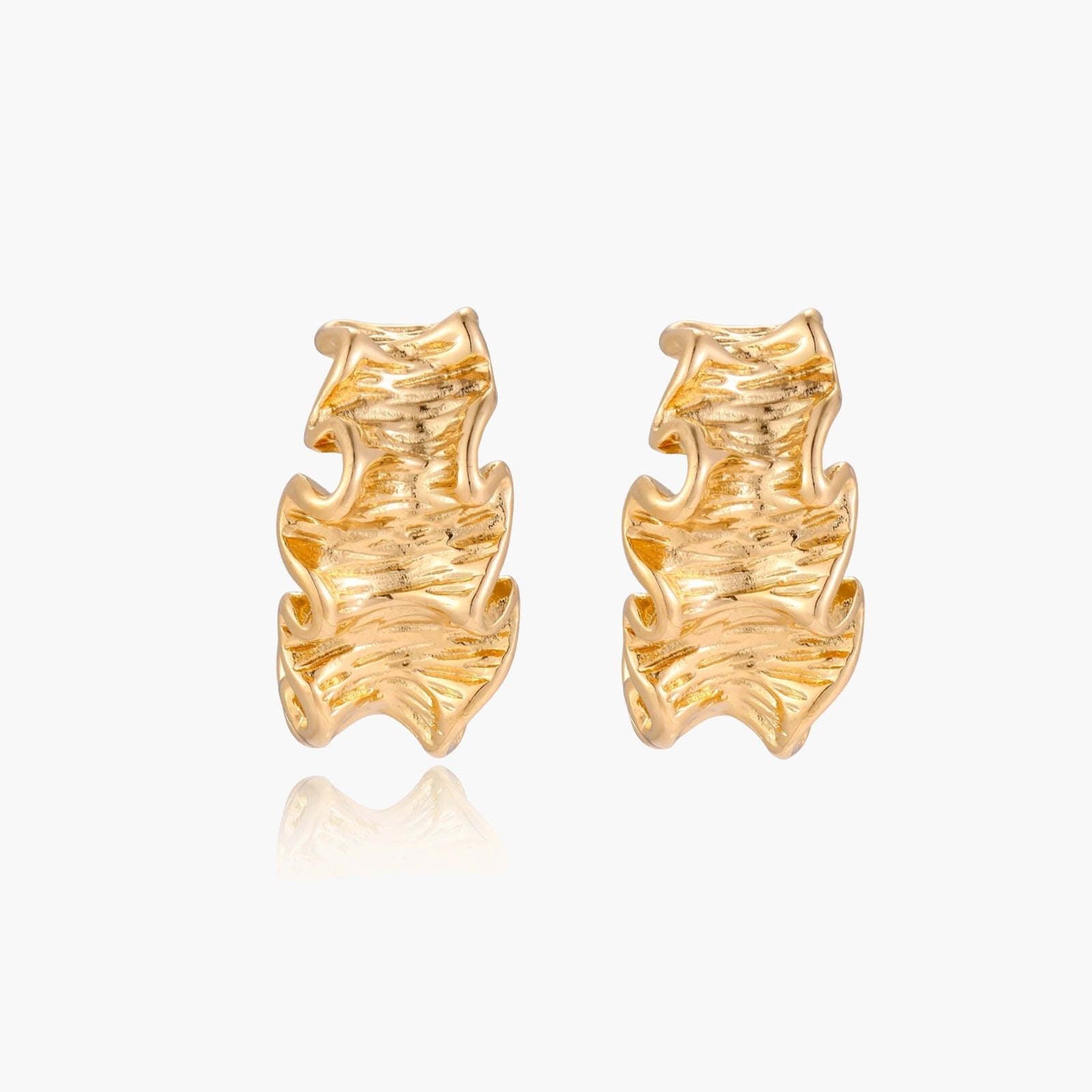 Pair of gold huggie hoops with sculpted wave texture and dimensional ripples on neutral background.